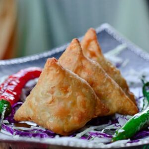 Crispy Indian samosas served with chili peppers and cabbage garnish.